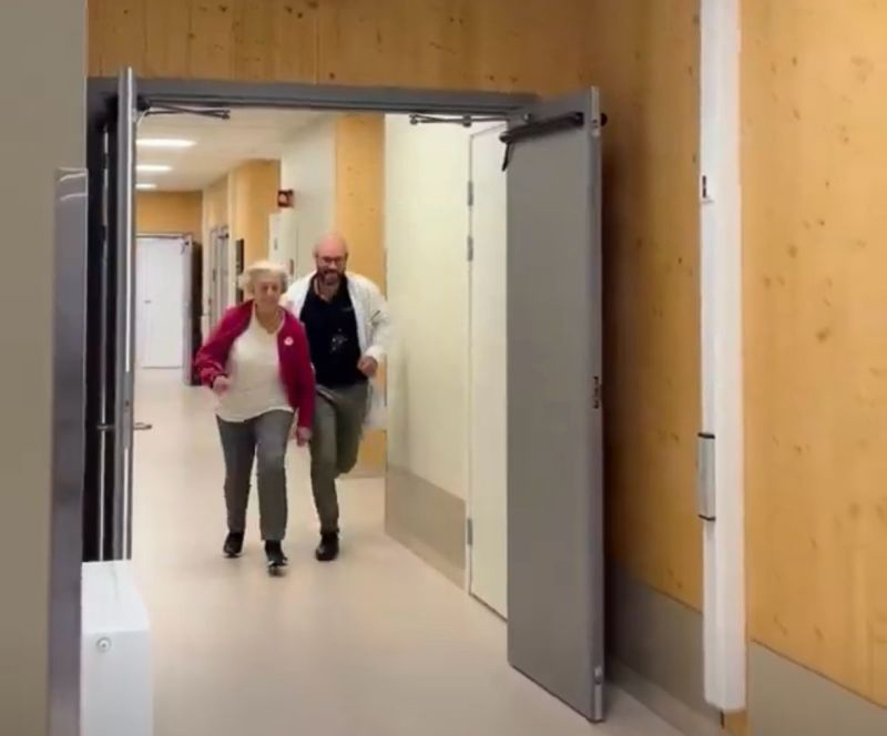 Sykehjemslege remi andersen løper i korridoren på oksenøya sykehjem sammen med beboer gunnvor på 92.